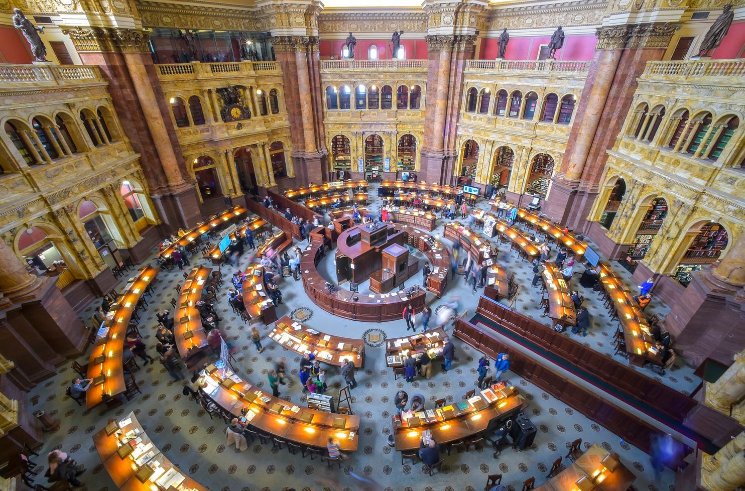 An 3/4 overhead view of the Library of Congress reading room, showing a concentric circles of reading desks and a high dome ceiling